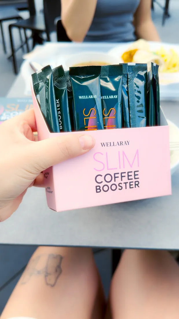 Hand hält die rosa Slim Coffee Booster Box mit Sticks im Café